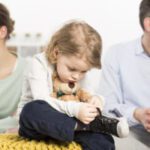 Child holding teddy bear, parents in background.