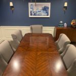 A long table with grey chairs in front of a blue wall.