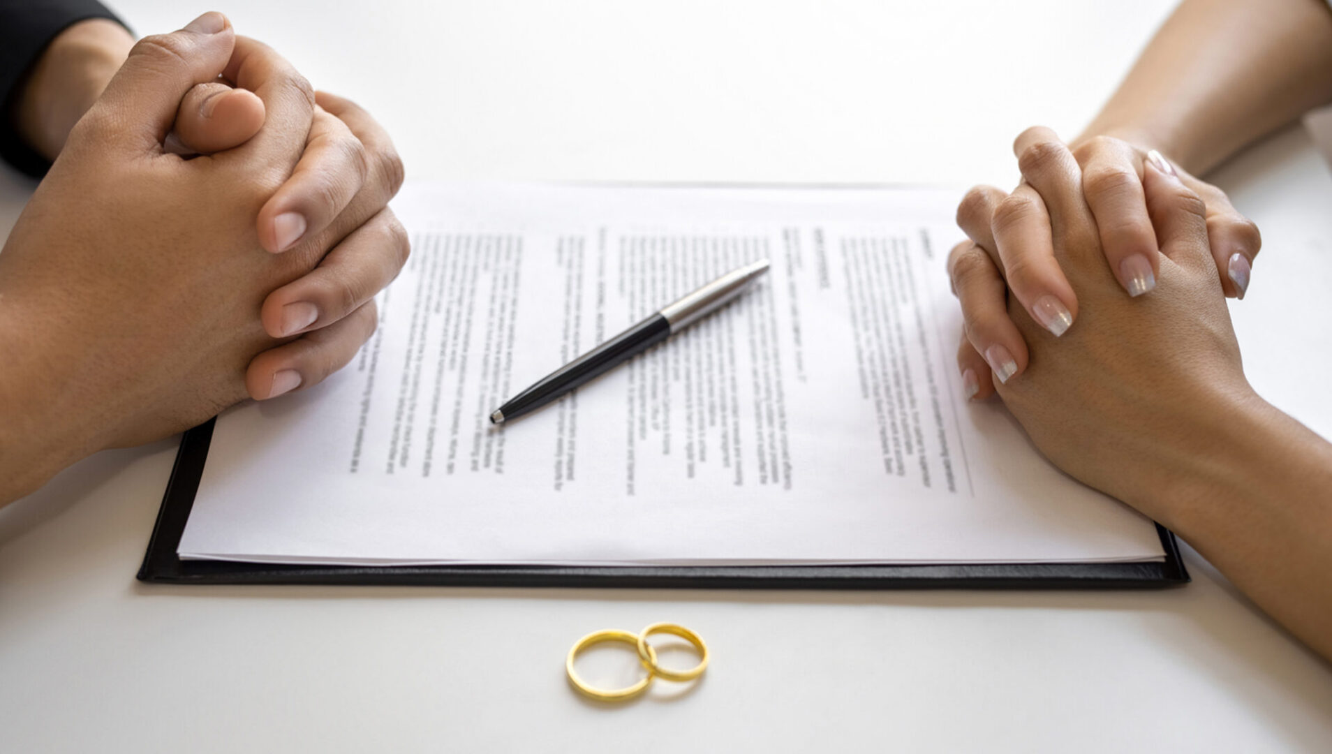 Hands, divorce papers, pen, and wedding rings.