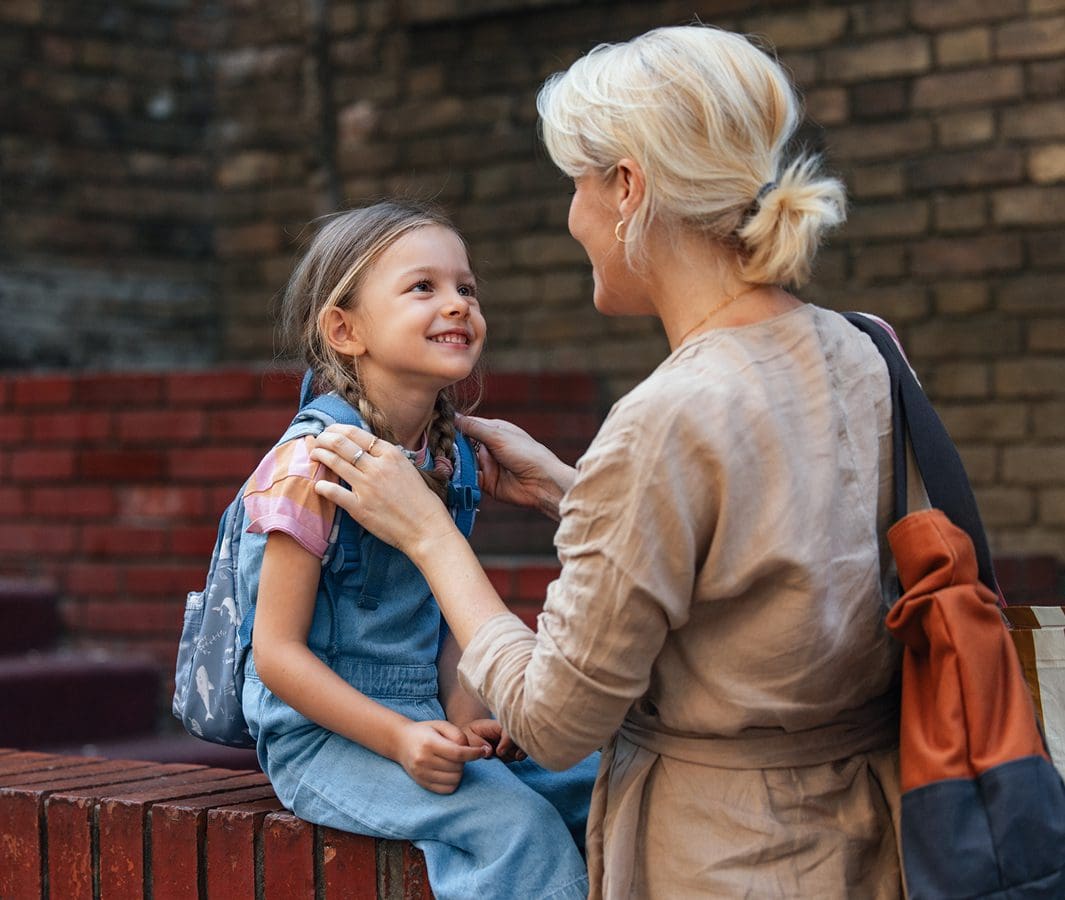 Adult and child smiling outside near bricks.